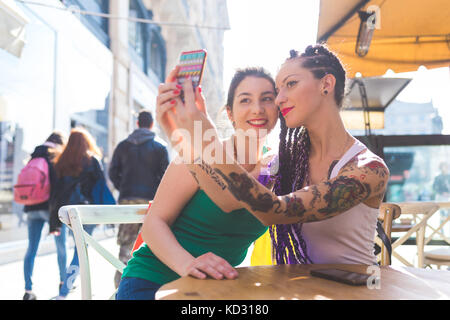 Les femmes sur city break at outdoor cafe en tenant, Milan, Italie selfies Banque D'Images