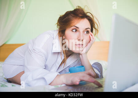 Jeune femme agenouillée sur bed using laptop Banque D'Images
