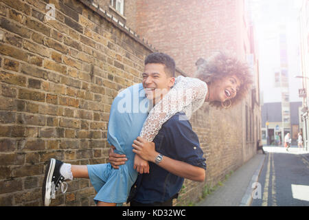 Jeune couple de jouer dans la rue, man carrying woman over shoulder Banque D'Images