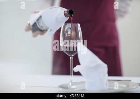 Serveur dans un restaurant de verser un verre de vin rouge, mid section Banque D'Images