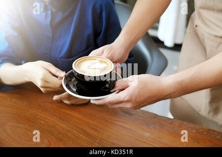 Close-up part d'une serveuse de servir une tasse de café au client. focus sélectif. Banque D'Images