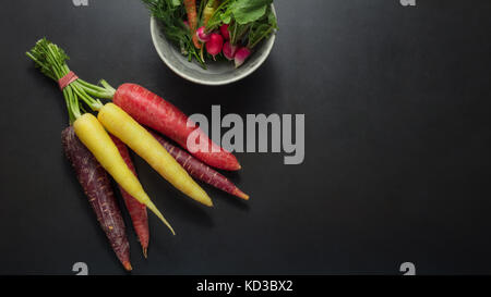 Les radis et les carottes colorées regroupé sur la table à côté un bol les feuilles d'aneth, les épinards et les radis. Banque D'Images