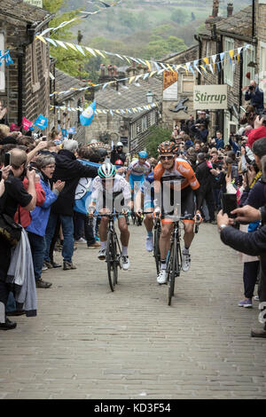 Les coureurs du Tour de Yorkshire monter la rue Main à Haworth, West Yorkshire Banque D'Images