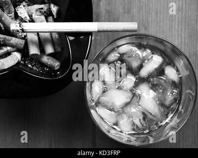 Imaqge monochrome noir et blanc d'un verre de whisky écossais et d'une cigarette allumée sur un cendrier Banque D'Images