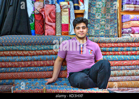 La province du Fars, Shiraz, Iran - 19 avril, 2017 : un jeune homme iranien vendeur est assis en face de ses marchandises dans un magasin de tissu. Banque D'Images