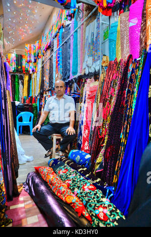 La province du Fars, Shiraz, Iran - 19 avril, 2017 : un vendeur iranien inconnu se dresse au milieu de tissus colorés et lumineux, dans la boutique de textile de la ville bazar. Banque D'Images