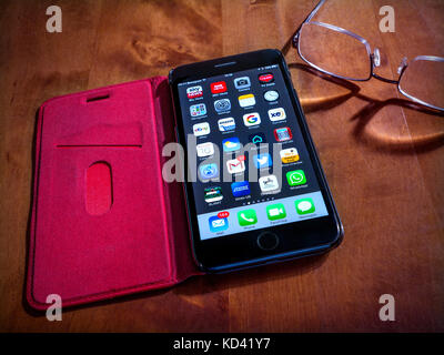 Smartphone apps iPhone 7 plus Noir avec applications écran, dans étui folio en cuir rouge sur table, avec lunettes de lecture sur le côté. Banque D'Images