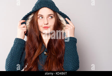 Une belle femme heureuse avec des cheveux longs en tricot chaud vêtu d'un sweat-shirt bleu-vert ou un manteau avec une capuche réchauffé avec fourrure blanche. fille lève les yeux. Banque D'Images