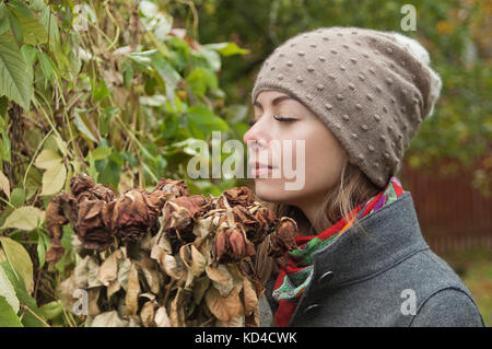 Jeune femme sentant un bouquet de roses fanées, un parc d'automne dans l'arrière-plan flou Banque D'Images