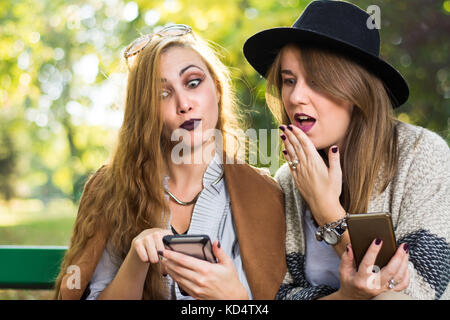 Amis féminins commérages avec un téléphone dans le parc Banque D'Images