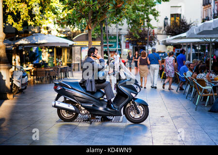 Bel homme en costume sur son téléphone portable assis sur un scooter à Madrid Banque D'Images