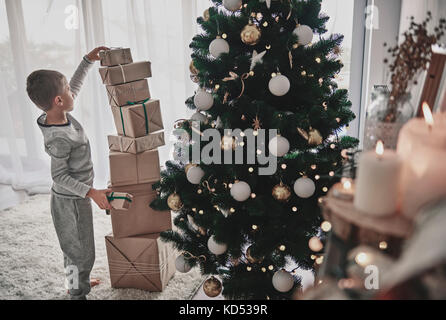 Boy stacking des cadeaux de Noël à côté d'un arbre de Noël Banque D'Images