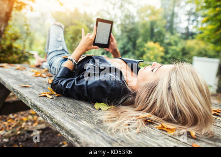 Fille blonde lire ebook allongé sur une table en bois à l'automne parc. Banque D'Images