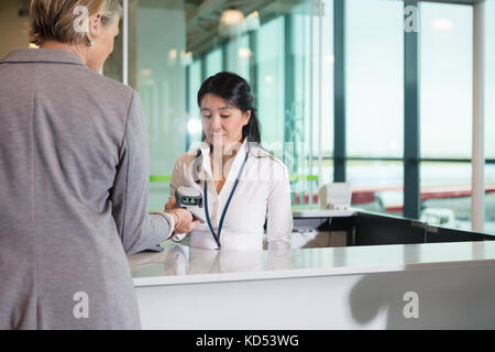 Mid adult réceptionniste Barcode scanning sur téléphone mobile détenu par businesswoman at counter in airport Banque D'Images