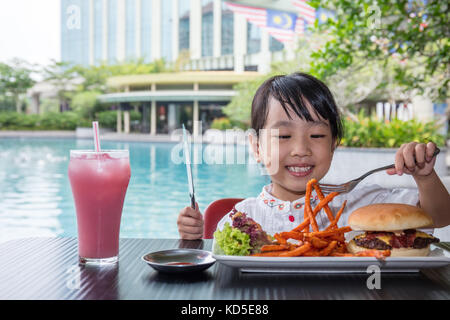 Peu asiatique chinese girl eating hamburger et frites au café en plein air Banque D'Images