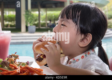 Peu asiatique chinese girl eating hamburger et frites au café en plein air Banque D'Images