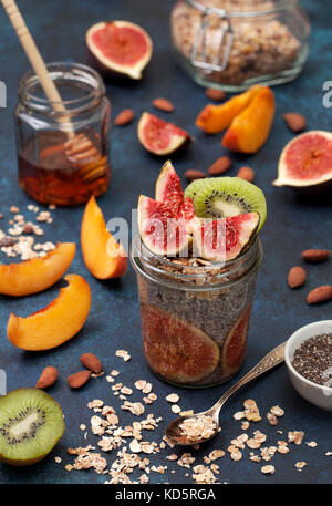 Petit déjeuner sain. chia pudding aux figues dans un bocal de verre, pêche, kiwi, amandes sur un fond bleu Banque D'Images