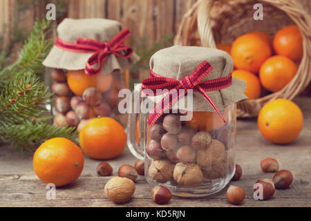 Cadeaux de Noël dans un bocal en verre : noix, noisettes, mandarines sur le vieux fond de bois Banque D'Images