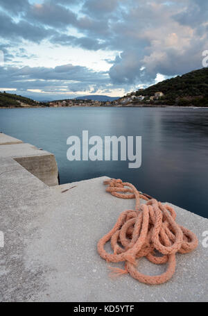 Un séjour relaxant et apaisant seascape avec un morceau de corde enroulé sur un mur du port avec vue sur le port dans la ville grecque de kassiopi sur Corfou. Banque D'Images