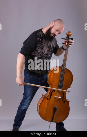 Le violoncelliste jouant la musique classique au violoncelle. barbu de jouer avec un instrument de musique sur fond gris Banque D'Images