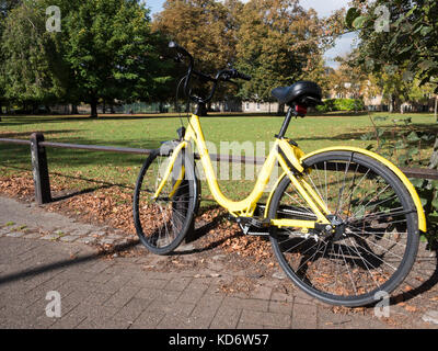 Location de voitures OFO jaune ou un vélo appuyé contre une rambarde dans un parc à Cambridge UK Banque D'Images