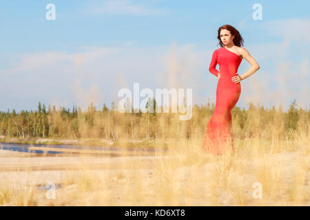 Dame dans une robe rouge d'un séjour entre l'herbe d'automne Banque D'Images