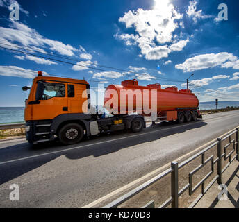 L'orange road tanker se déplace le long de la route sous les nuages et le ciel bleu Banque D'Images