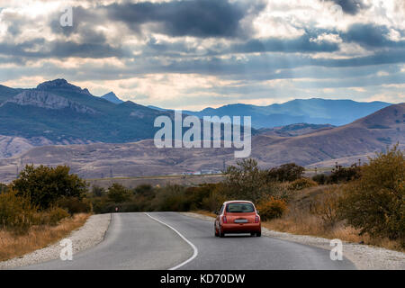 La voiture rouge se déplace le long de la route, autour d'un beau paysage. le bleu des montagnes tonitruant sous le ciel couvert de nuages Banque D'Images