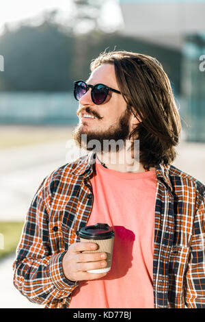Portez des lunettes de soleil homme hipster beau café tasse avant détient un immeuble moderne Banque D'Images