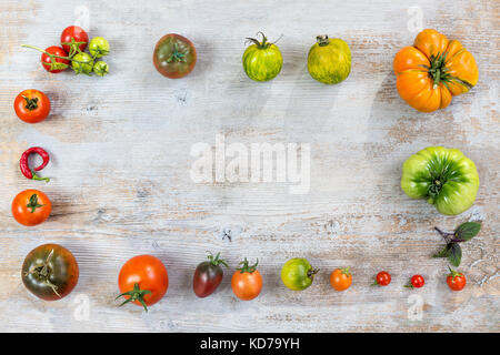 Châssis de différentes matières organiques couleur homegrown tomatoes on ancienne en bois peint en arrière-plan. avec fond rouge, jaune, orange et vert les tomates. La nourriture végétarienne saine concept. copie espace. Vue de dessus Banque D'Images