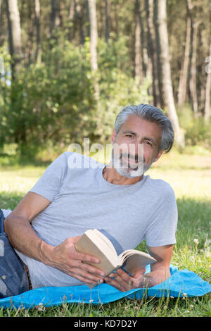 Homme lyingsitting dans l'herbe lire un livre Banque D'Images