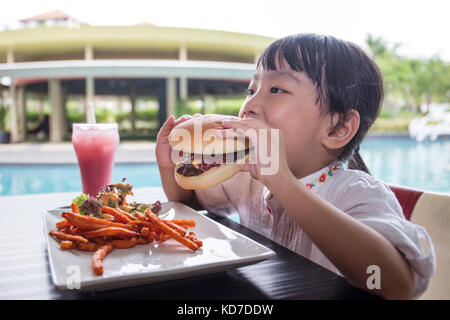 Peu asiatique chinese girl eating hamburger et frites au café en plein air Banque D'Images