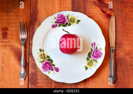 L'un venu pomme rouge sur plaque avec fourchette et couteau sur fond de bois Banque D'Images