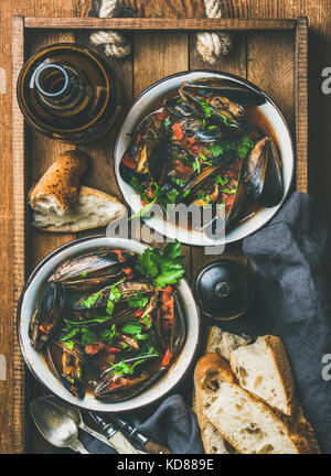 Télévision à jeter des moules bouillies belge à la sauce tomate avec du persil dans les cuves métalliques servant de plateau en bois, des tranches de baguette de pain et de la bière en bouteille Banque D'Images