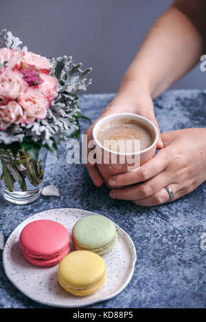 Femme tenant une tasse de café et manger macarons pour le dessert Banque D'Images