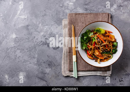 Faire sauter les nouilles Udon avec la viande de poulet et de légumes dans le bol sur fond de béton copy space Banque D'Images