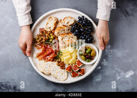 Des en-cas italiens de la nourriture avec du jambon, olives, fromage, tomates séchées, saucisses et Pain dans les mains des hommes sur fond de béton Banque D'Images