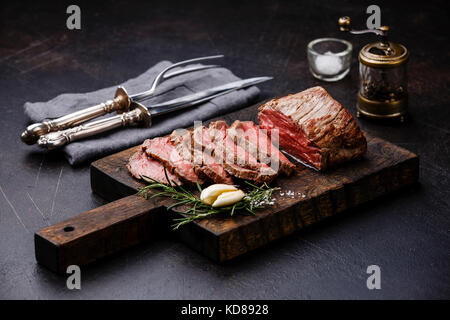 Filet de bœuf Rôti de viande en tranches sur une planche à découper avec couteau et fourchette, ensemble de moulin à poivre et saltcellar Banque D'Images