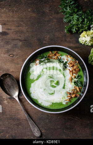 Soupe crème de brocoli végétarien servi en noir bol avec cuillère, crème, oignon frit, persil frais et brocoli au vieux fond de bois. Vue supérieure de la wi Banque D'Images