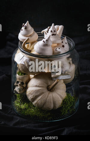 Dessert sucré Halloween décoration de table blanc avec bol en verre de fantômes à la meringue avec les yeux chocolat décor, crânes, Moss et de citrouille sur fond noir. Banque D'Images