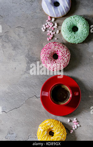 Variété de beignes glacés colorés avec du sucre rose et tasse de café noir rouge gris sur fond de texture. Mise à plat avec l'espace Banque D'Images