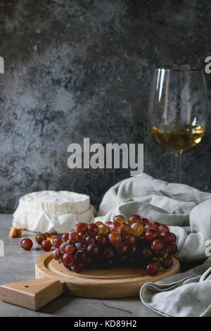 Bouquet de raisin rouge, camembert, croûtons et verre de vin blanc servi sur sol en bois servant de sélection sur table de cuisine gris. Style rustique. Banque D'Images