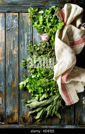 Variété de produits frais biologiques herbes coriandre, sauge, origan et l'ail avec cuisine textiles serviette sur vieille planche en bois. Vue supérieure avec spa de copie Banque D'Images