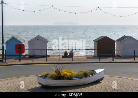 Couple de plage, vue arrière d'un couple d'âge moyen assis seul entre des cabanes de plage sur le front de mer à Felixstowe, regardant un bateau à conteneurs éloigné, Royaume-Uni Banque D'Images