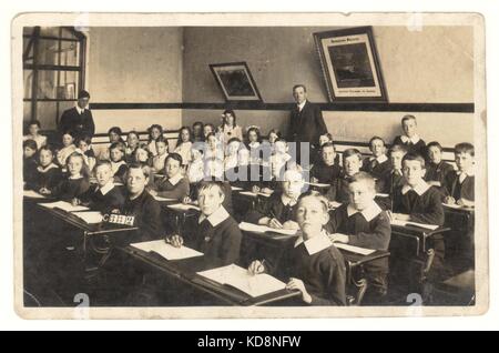 Carte postale édouardienne de junior school enfants - garçons et filles, en classe avec leur enseignant, vers 1910, au Royaume-Uni. Banque D'Images