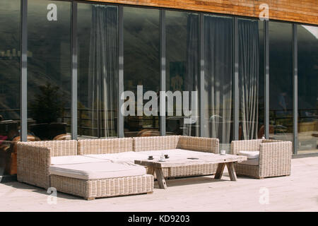 Des meubles en rotin sur balcon ensoleillé en journée d'été. accueil extérieur avec table, chaises et un canapé dans une terrasse en bois Banque D'Images