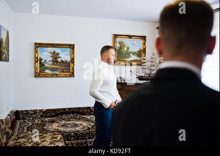 Portrait d'un beau palefrenier dressing up dans de spacieuses chambres de luxe et se préparer pour son grand jour de mariage et une groomsman debout dans le foregro Banque D'Images