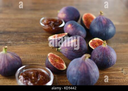 Bleu et violet figues mûres, les deux ensemble et les couper en deux, au hasard renversé sur la table en bois sombre entre les bols en verre de confiture de figues Banque D'Images