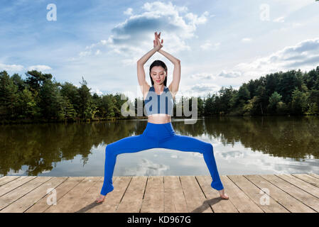 Woman practicing yoga à côté d'un lac, faire la déesse pose. Banque D'Images