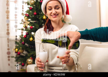 Cropped shot of man pouring champagne pour smiling young woman in santa hats Banque D'Images